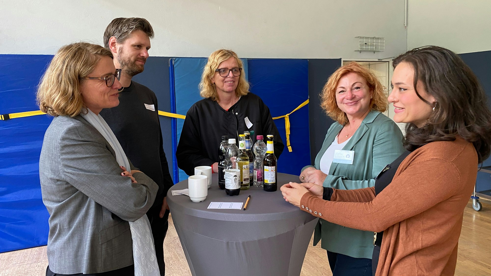 Vier Frauen und ein Mann stehen in einer Sporthalle an einem Tisch, auf dem Flaschen stehen.