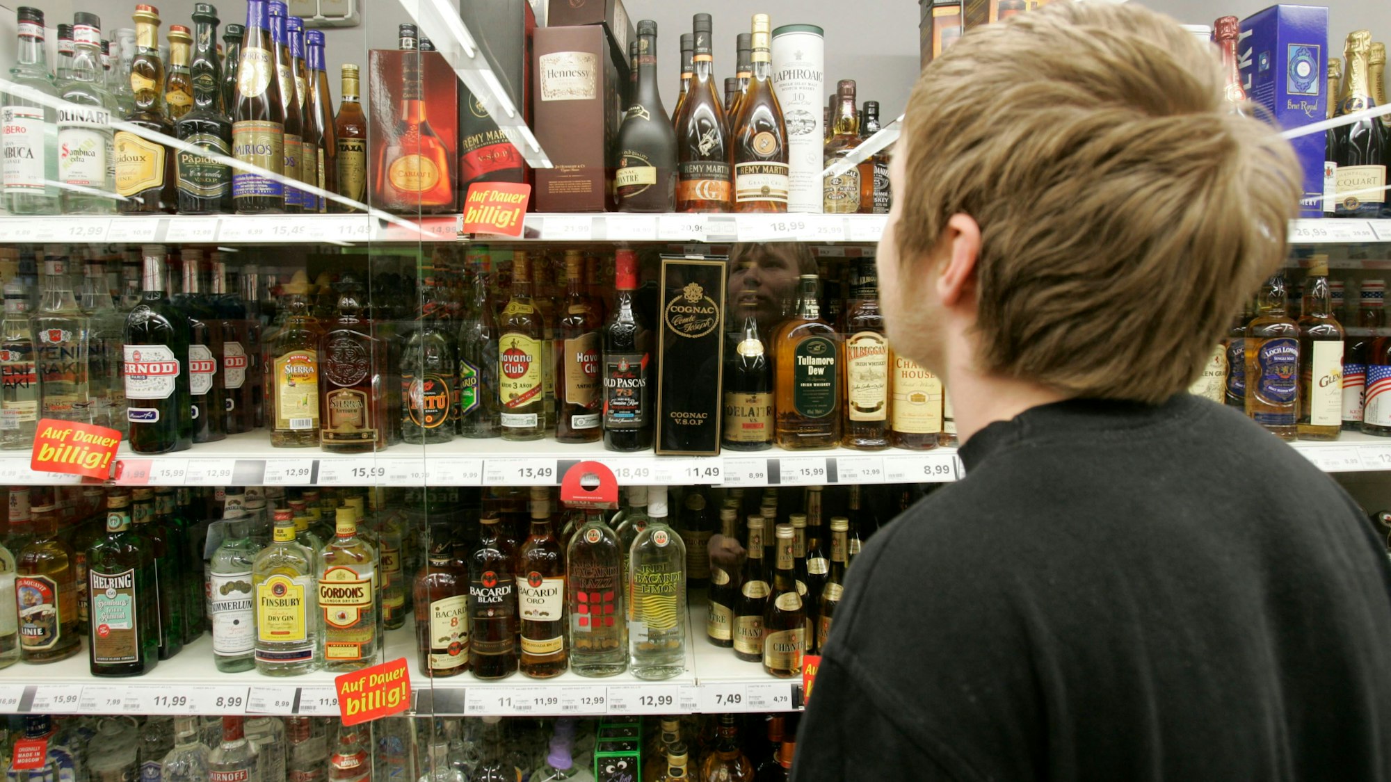 Ein junger Mann steht in einem Supermarkt in Bremen vor einem Spirituosenregal.