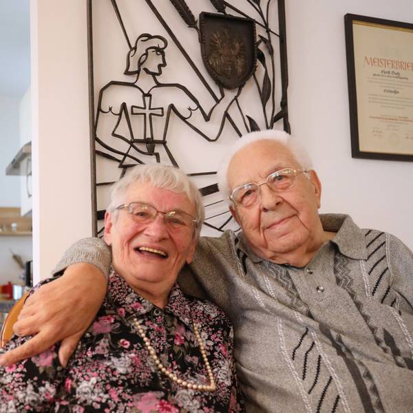 Ein Ehepaar sitzt eng beieinander, der Mann hat seinen Arm um seine Frau gelegt.