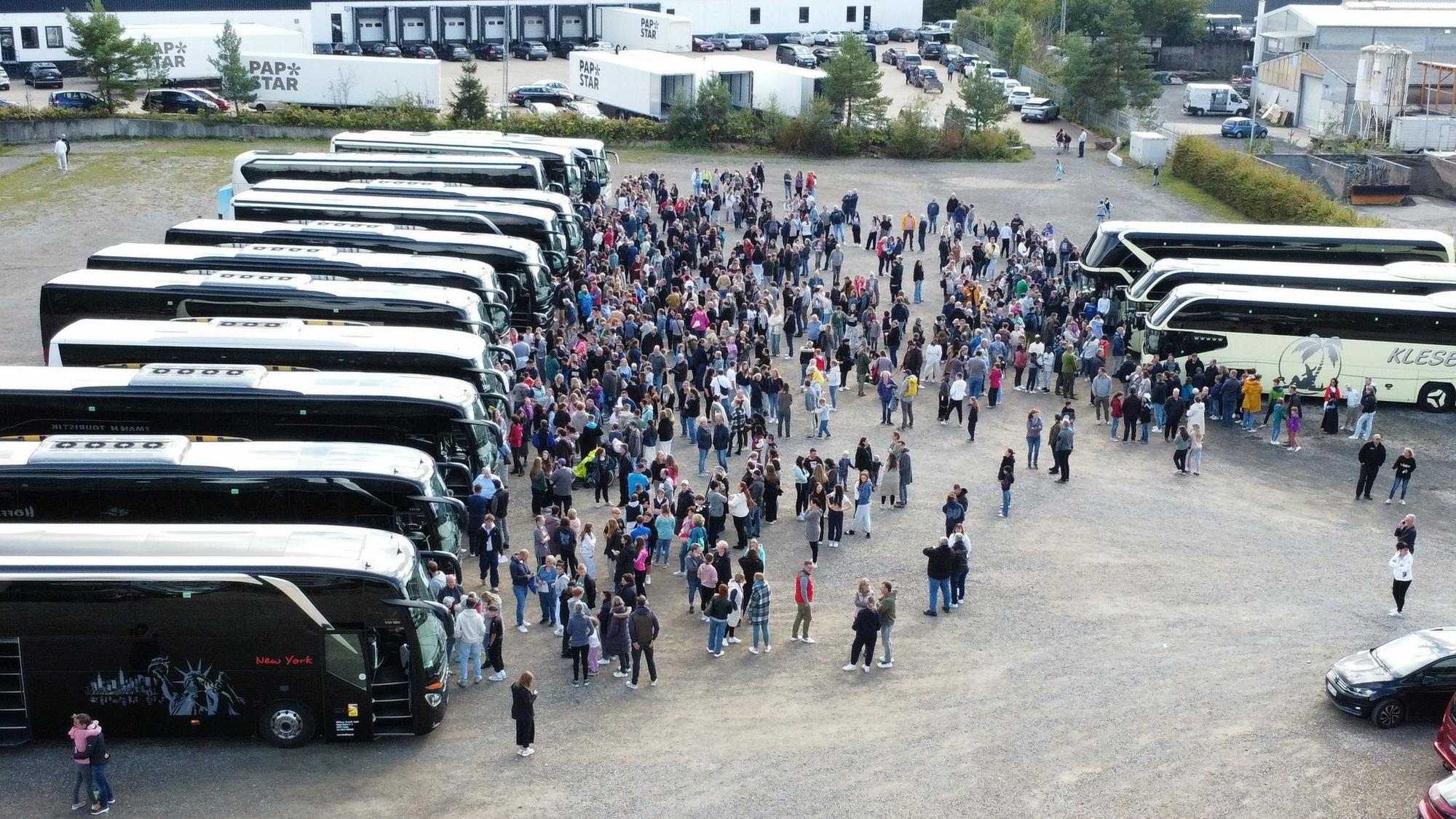 Blick von die nebeneinander stehenden Busse. Vor den Bussen ist ein Gewusel von Menschen zu sehen.