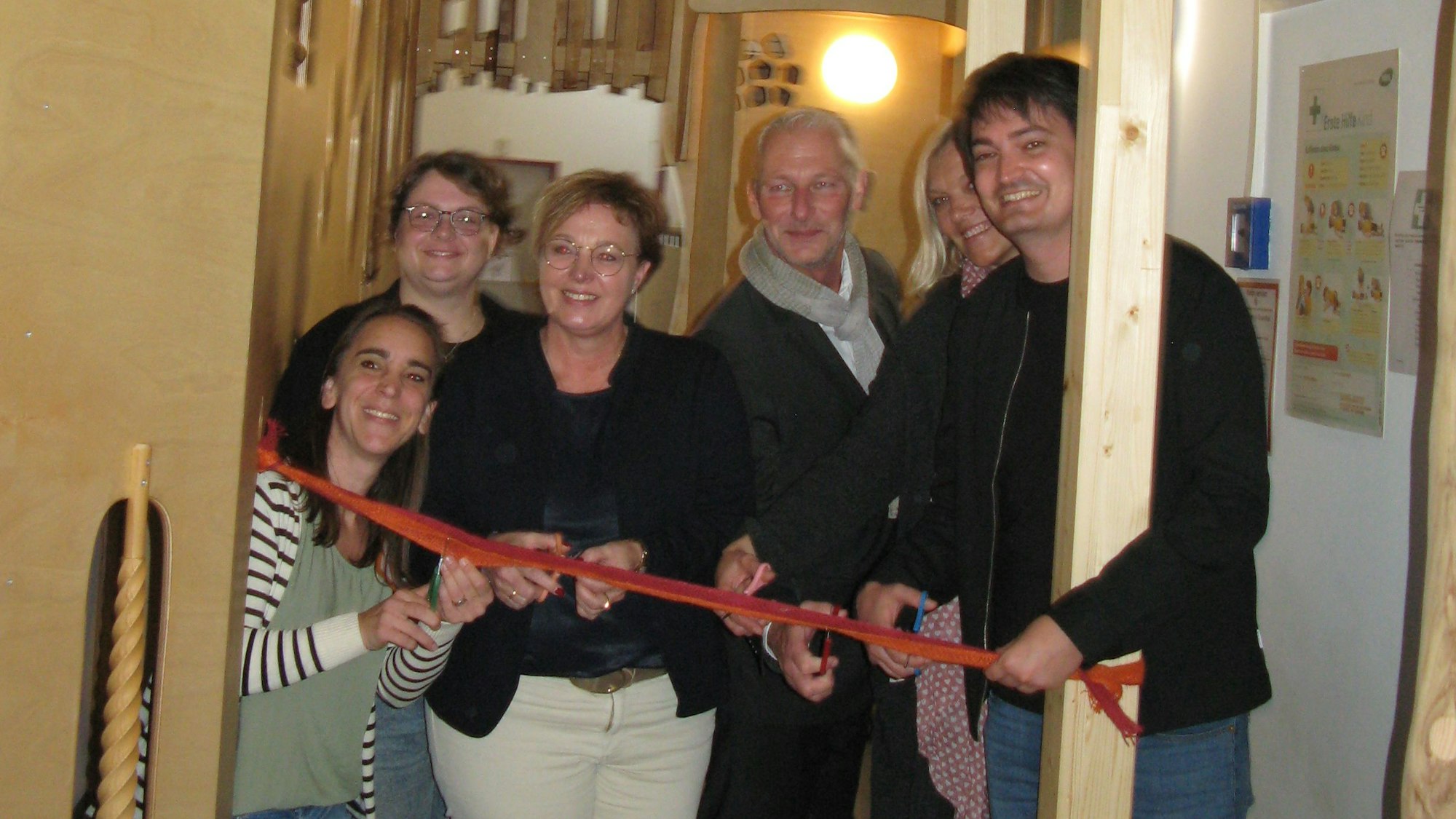 Vier Frauen und zwei Männer durchschneiden gut gelaunt mit Scheren ein rotes Band.