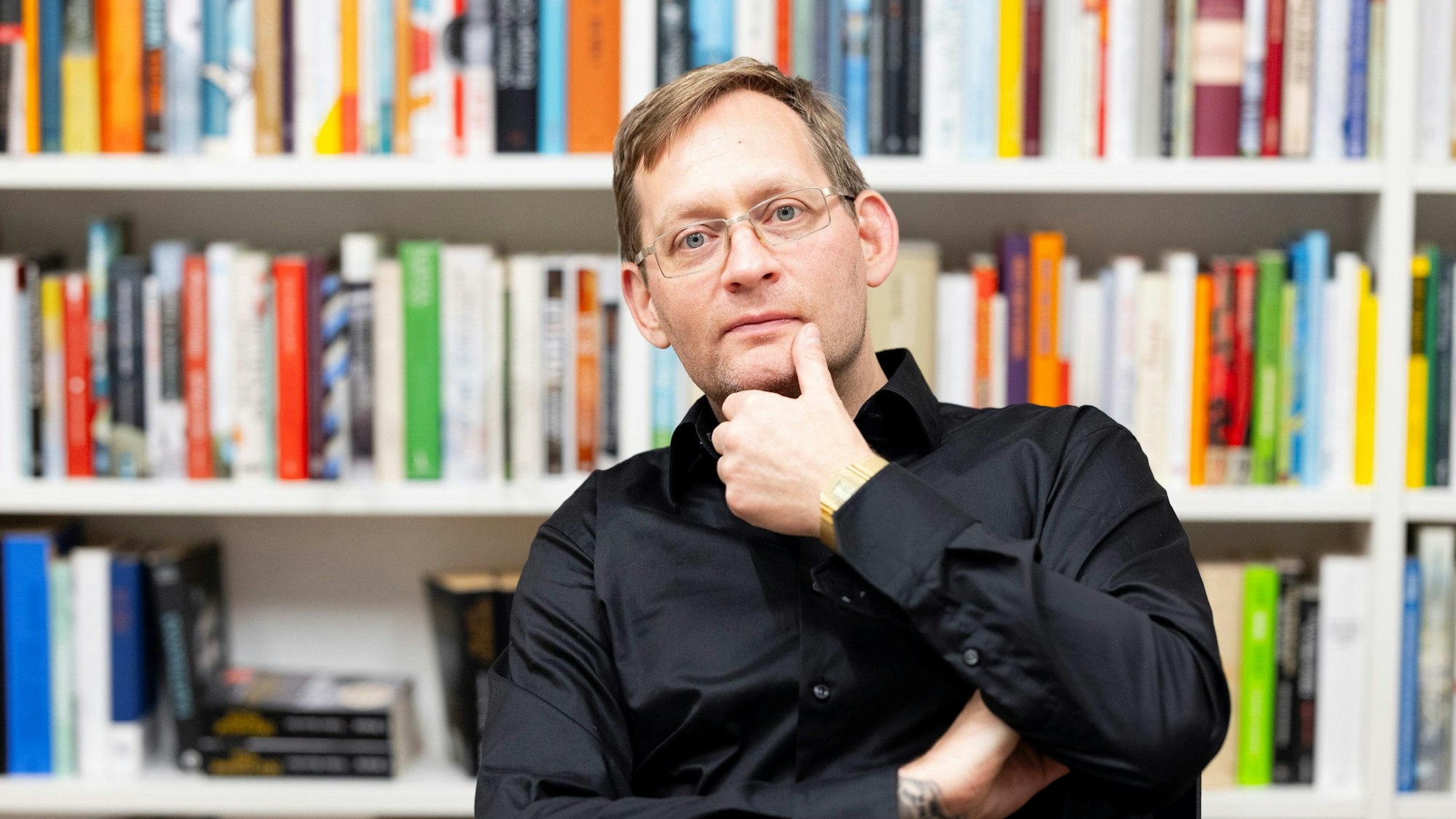Der Schriftsteller Clemens Meyer sitzt vor einem Bücherregal und schaut nachdenklich in die Kamera.
