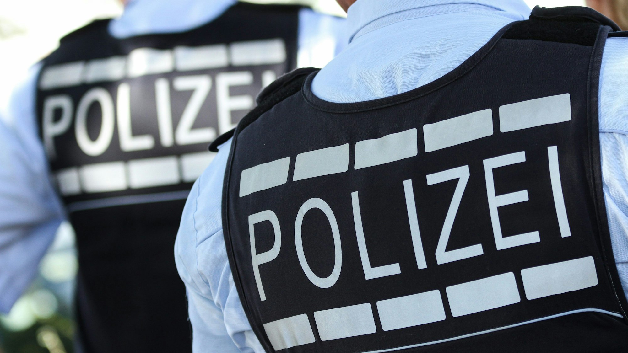 Das Symbolbild zeigt zwei Polizeibeamte von hinten mit der Aufschrift Polizei auf der Weste.