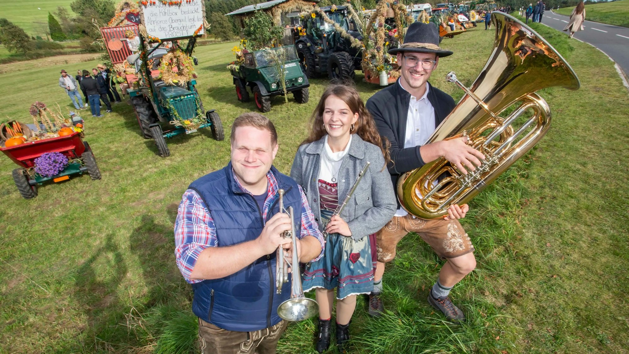 Zwei Musiker und eine Musikerin einer Blaskapelle stehen mit ihren Instrumenten auf einer Wiese.