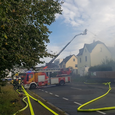 Von einer Drehleiter aus löschen Feuerwehrleute ein brennendes Haus.