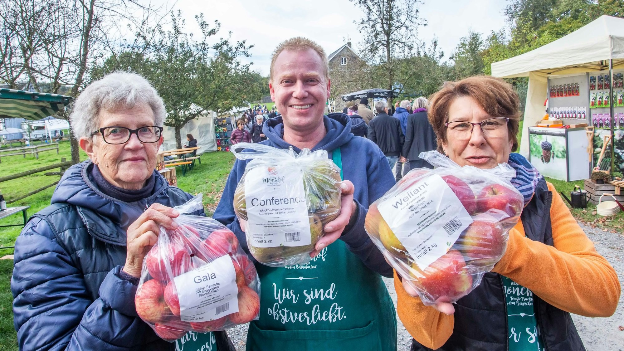 Zwei Frauen und ein Mann halten Säcke mit Äpfeln in den Händen.