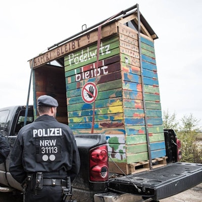 Auf dem Foto ist ein Baumhaus zu sehen, das auf einem Wagen abtransportiert wird. Dabei stehen Polizisten.