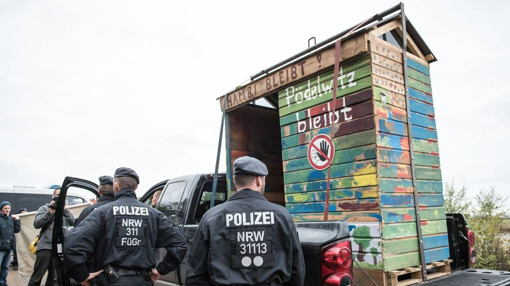 Auf dem Foto ist ein Baumhaus zu sehen, das auf einem Wagen abtransportiert wird. Dabei stehen Polizisten.