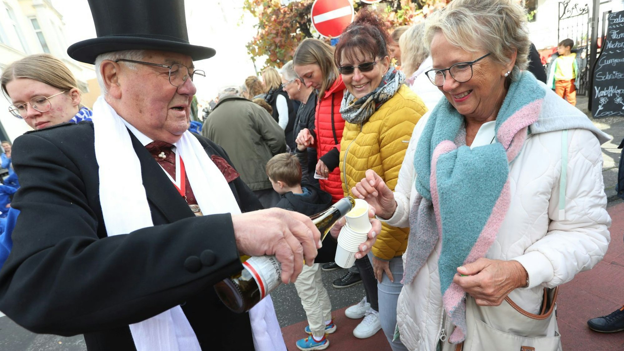 Ein Mann mit Zylinder auf dem Kopf schenkt einer Frau ein Glas Wein ein.