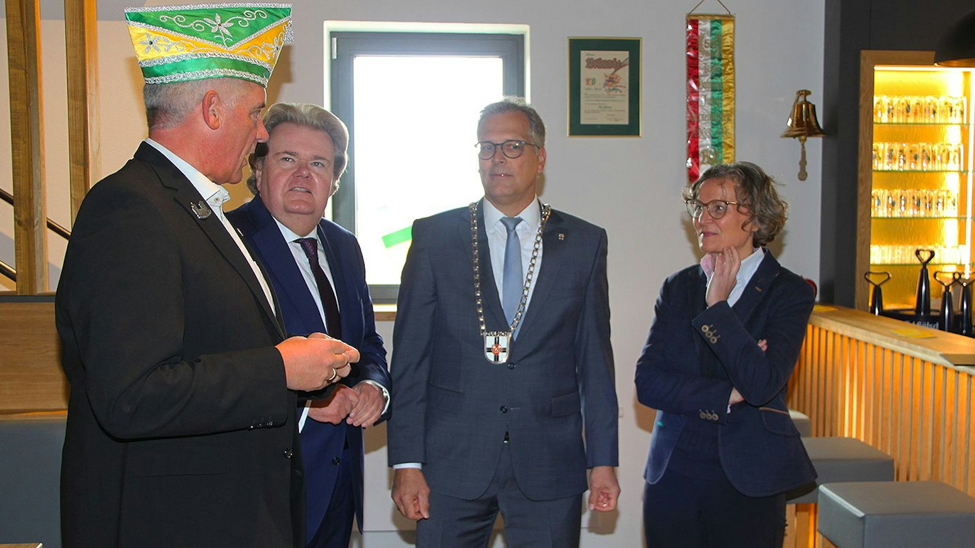 Drei Männer und eine Frau stehen miteinander redend vor einer Theke zusammen.