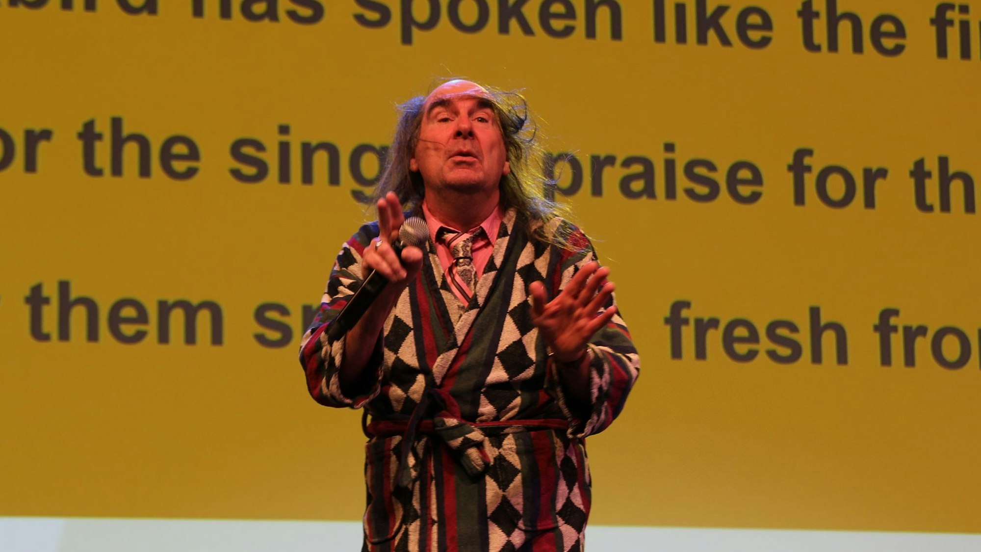 Guildo Horn auf der Bühne. Im Hintergrund wird auf einer Leinwand ein Liedtext eingeblendet, damit das Publikum mitsingen kann.