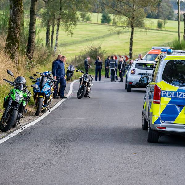 Ein Polizeiauto steht an einem Unfallort. Am Rand der Straße stehen mehrere Motorräder.