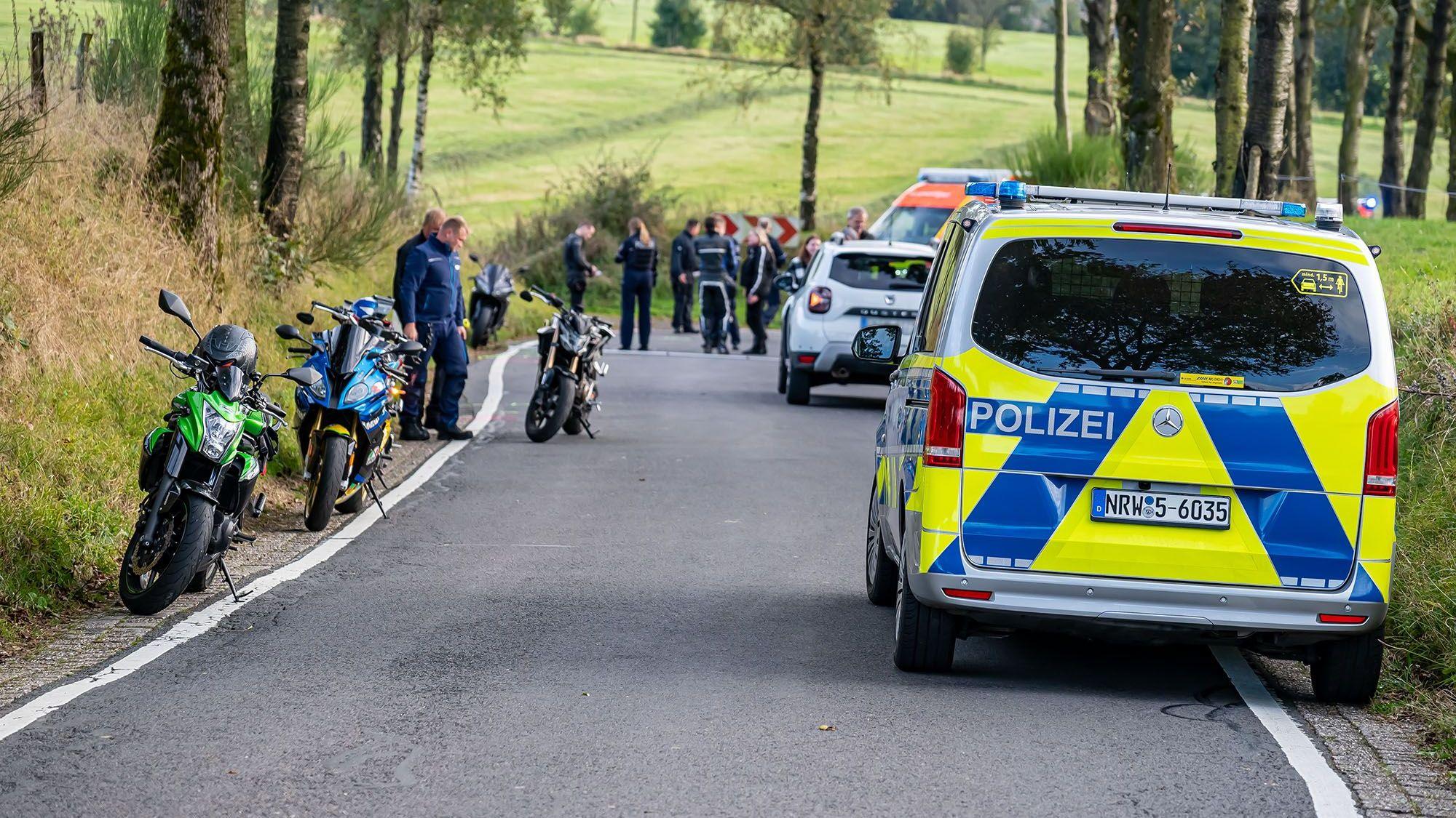 Ein Polizeiauto steht an einem Unfallort. Am Rand der Straße stehen mehrere Motorräder.