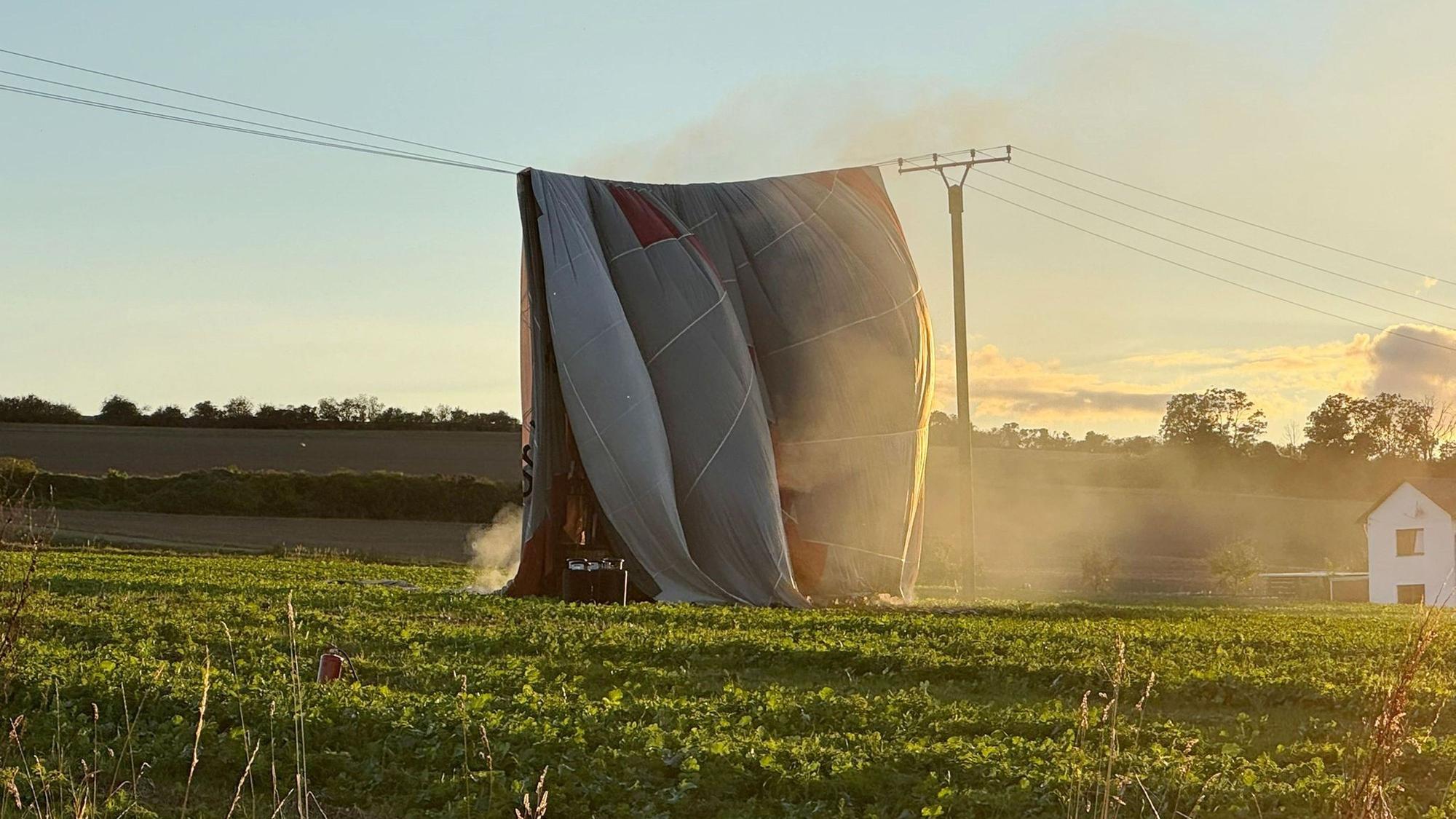 Die Hülle eines Heißluftballons, der auf einem Feld steht, ist über eine Stromleitung geweht worden.