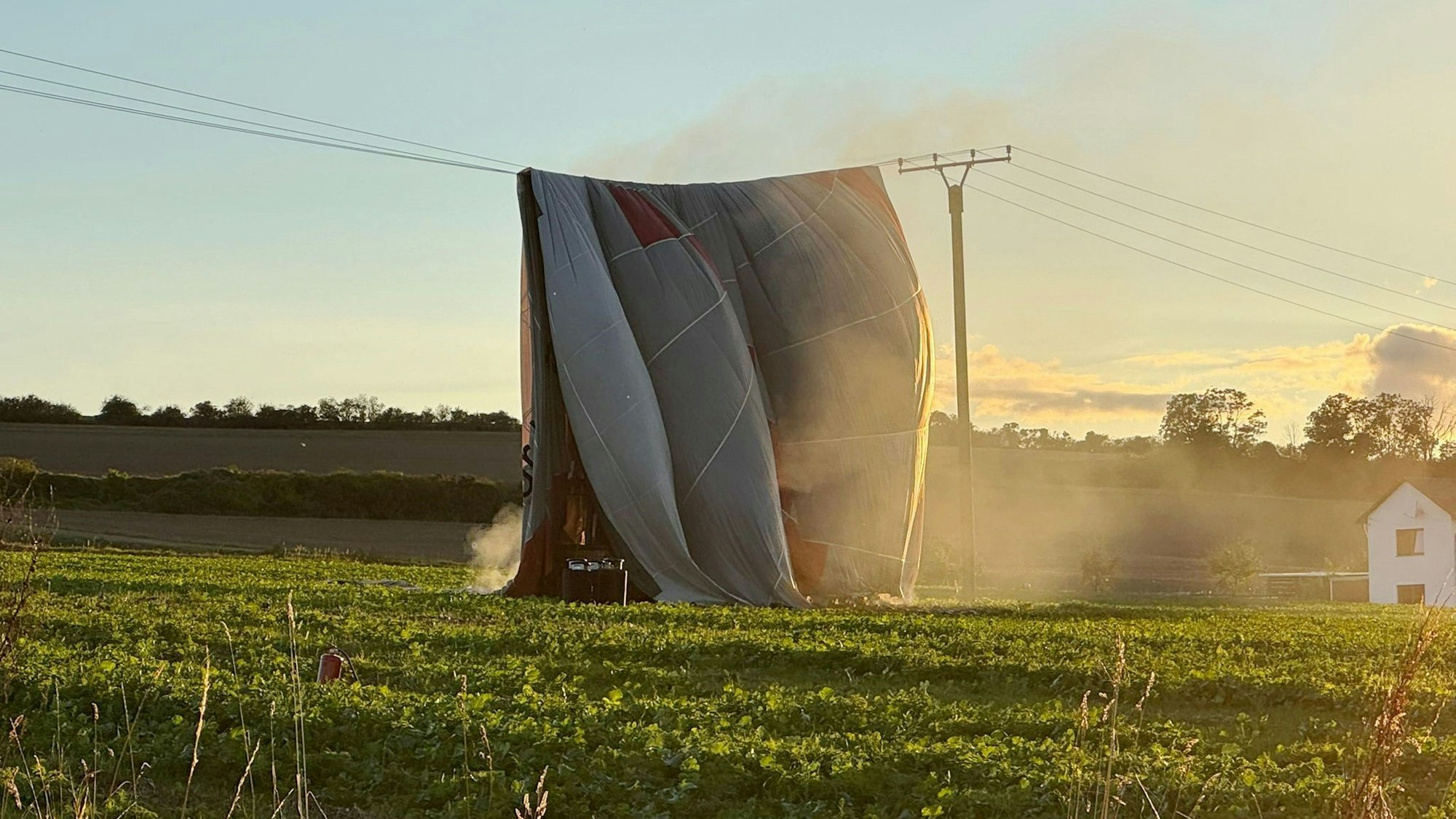 Die Hülle eines Heißluftballons, der auf einem Feld steht, ist über eine Stromleitung geweht worden.