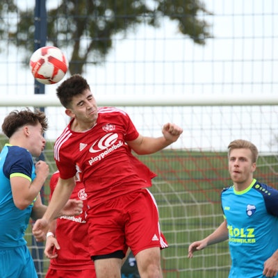 Zwei Spieler steigen zum Kopfballduell hoch, ein anderer beobachtet die Szene.