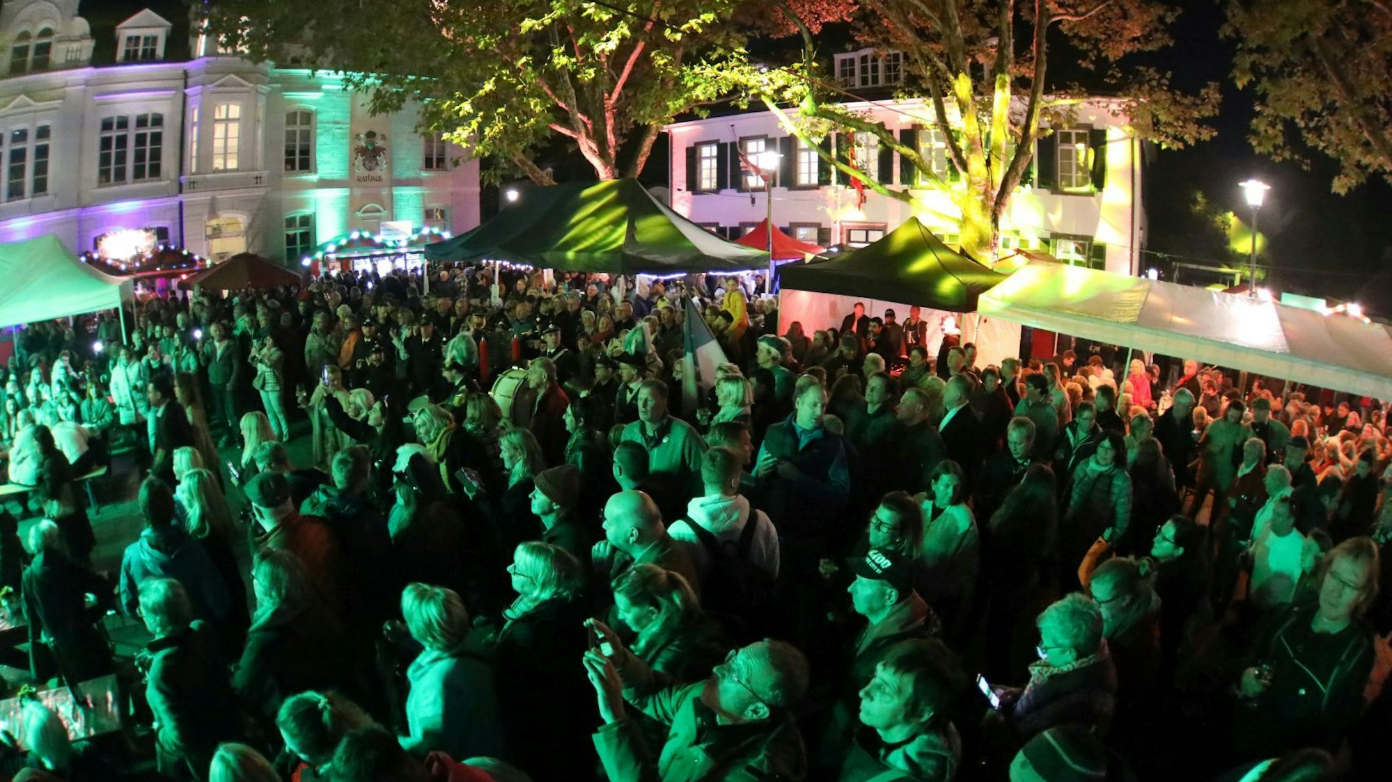 Eine in grünes Licht getauchte Menschenmenge, im Hintergrund Weinstände und ein historisches Gebäude.
