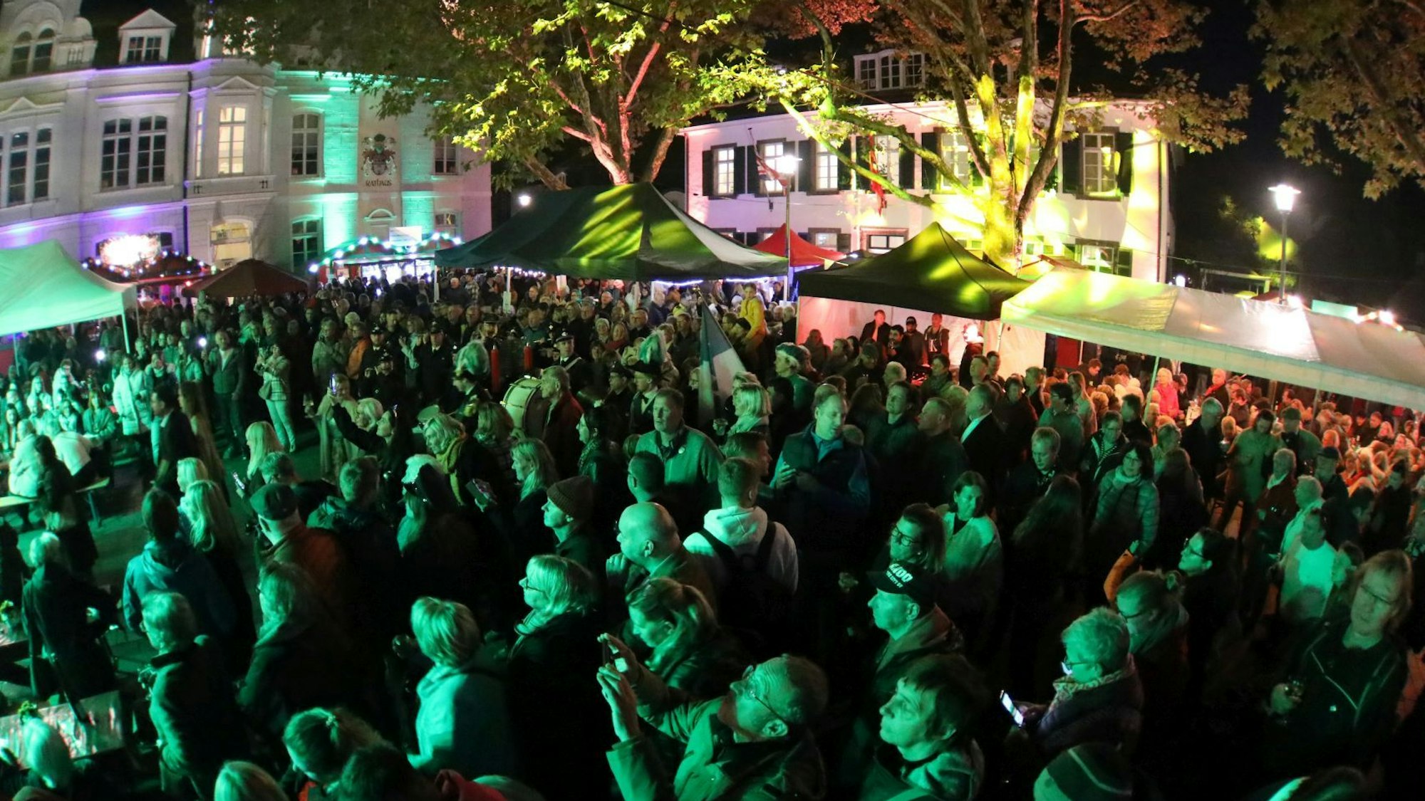 Eine in grünes Licht getauchte Menschenmenge, im Hintergrund Weinstände und ein historisches Gebäude.