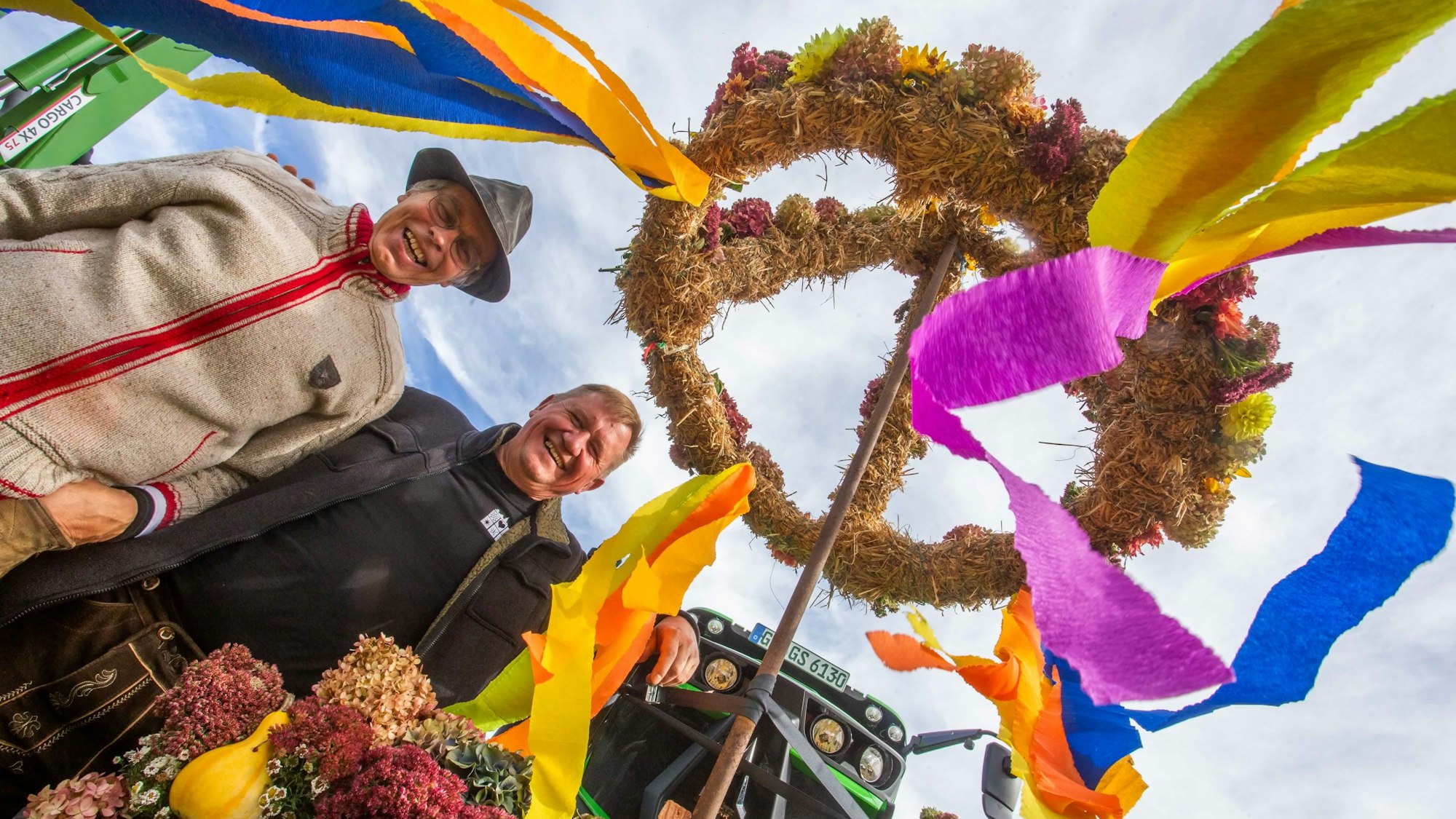 Zwei Männer stehen unter einem geschmückten Erntekranz.