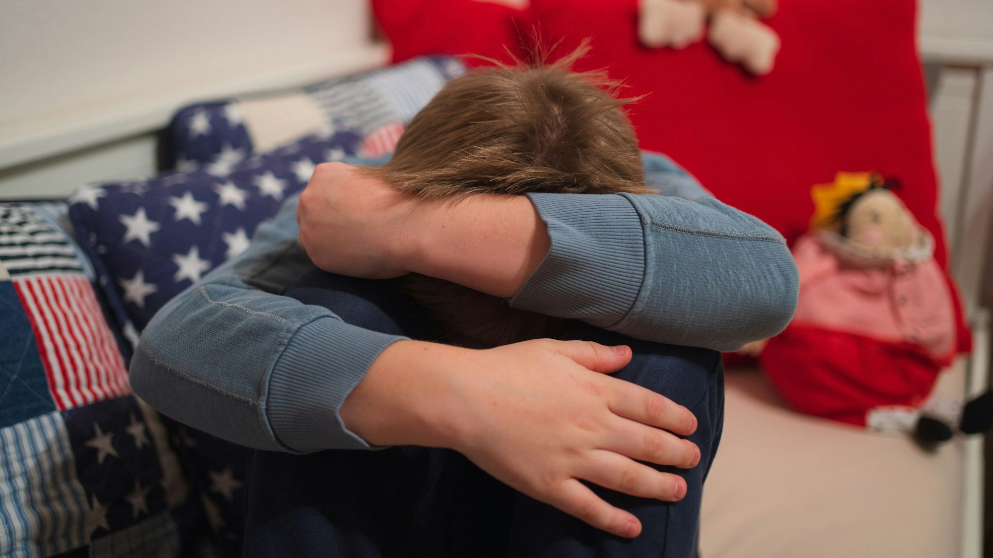 Ein Kind kauert sich auf seinem Bett zusammen.