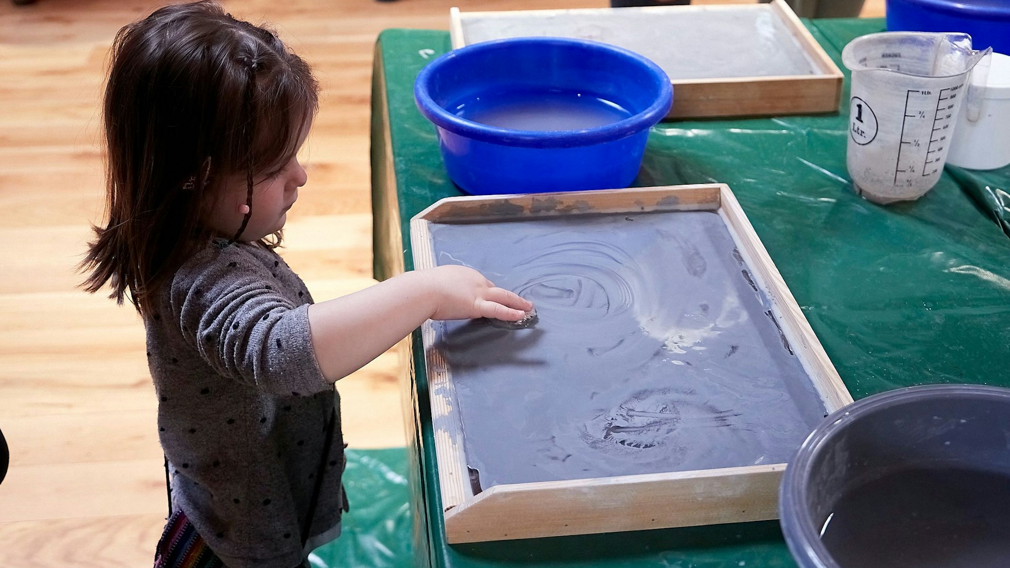 Ein kleines Kind steht an einem Tisch, darauf ein Holzbrett zum Fossilienschleifen.
