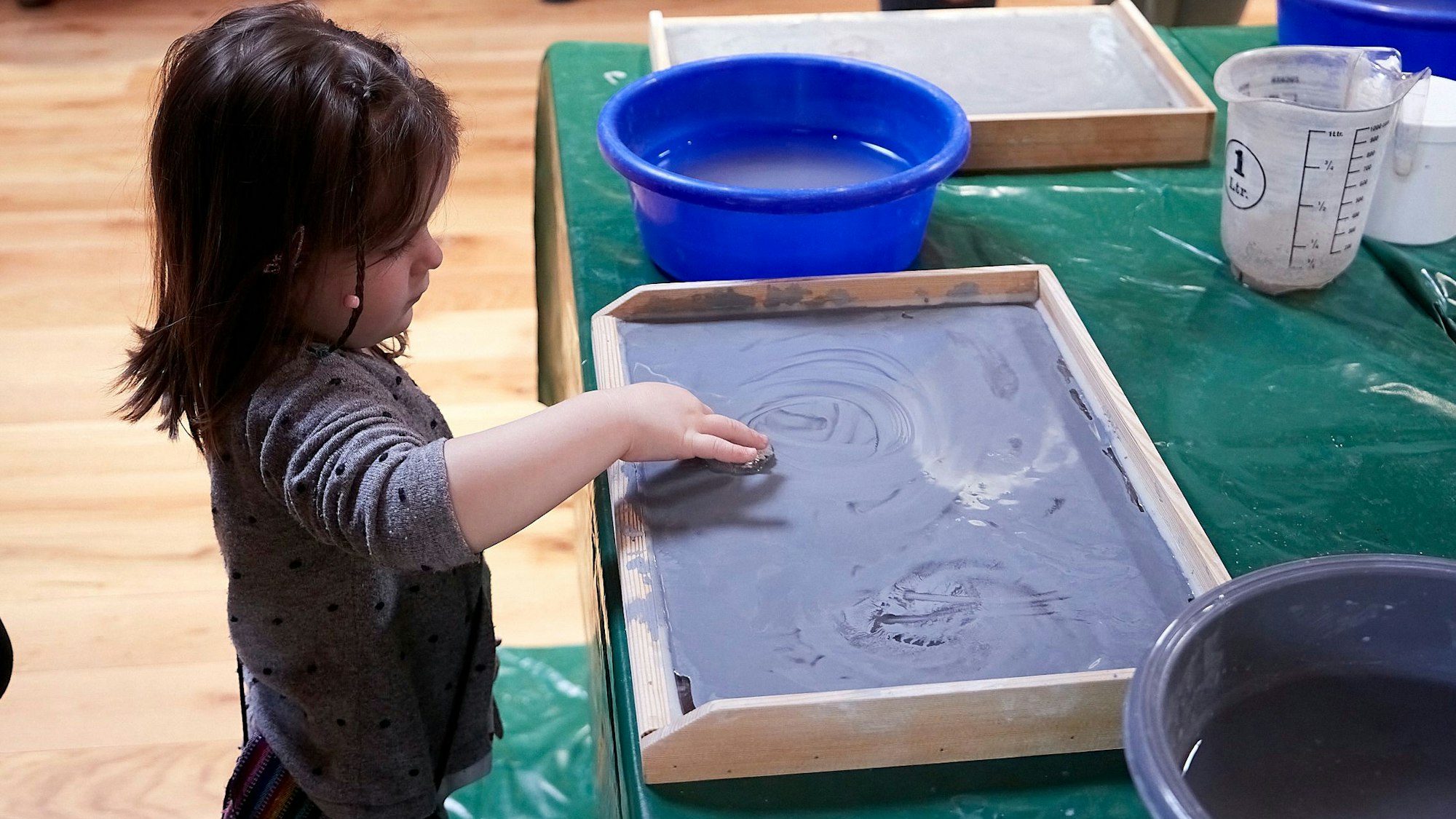 Ein kleines Kind steht an einem Tisch, darauf ein Holzbrett zum Fossilienschleifen.