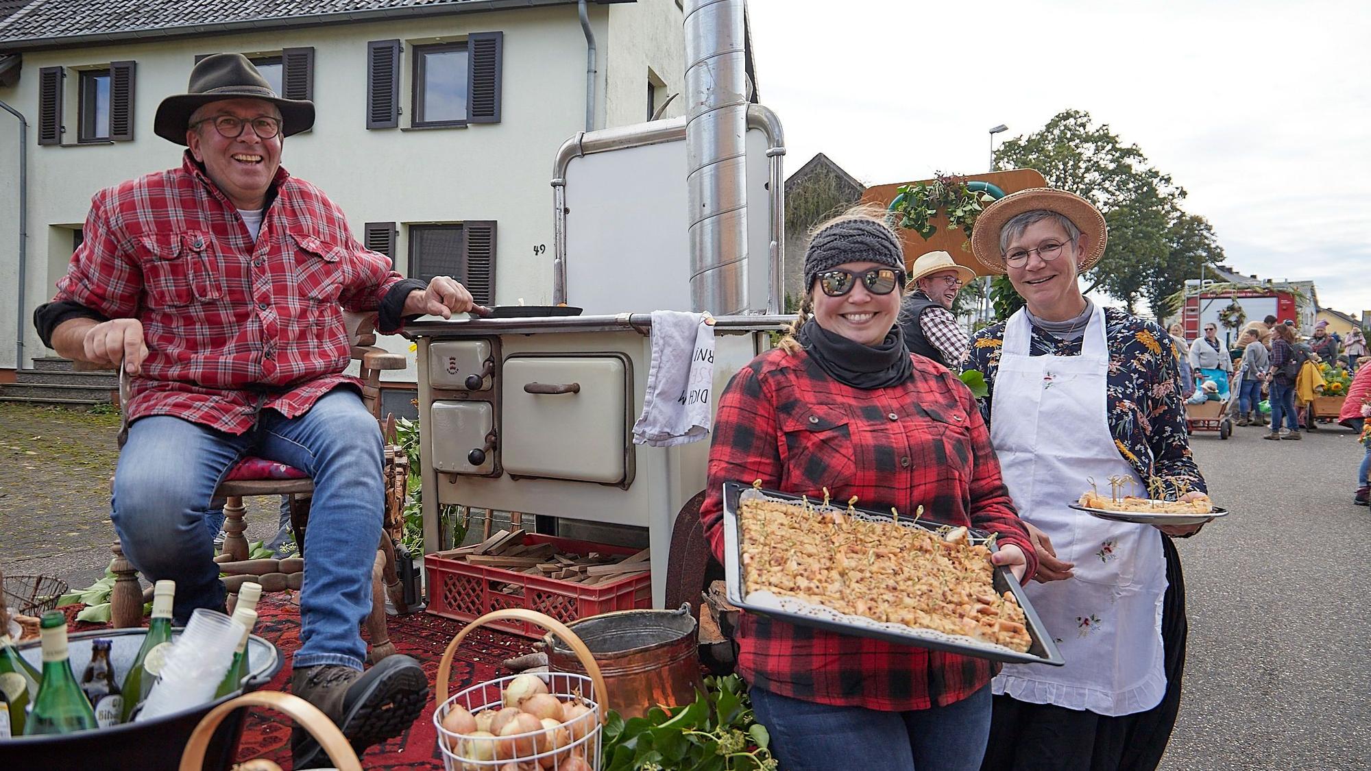 Ein Mann sitzt auf einem Stuhl, der auf einem Wagen steht, eine Frau präsentiert ein Blech mit Zwiebelkuchen.