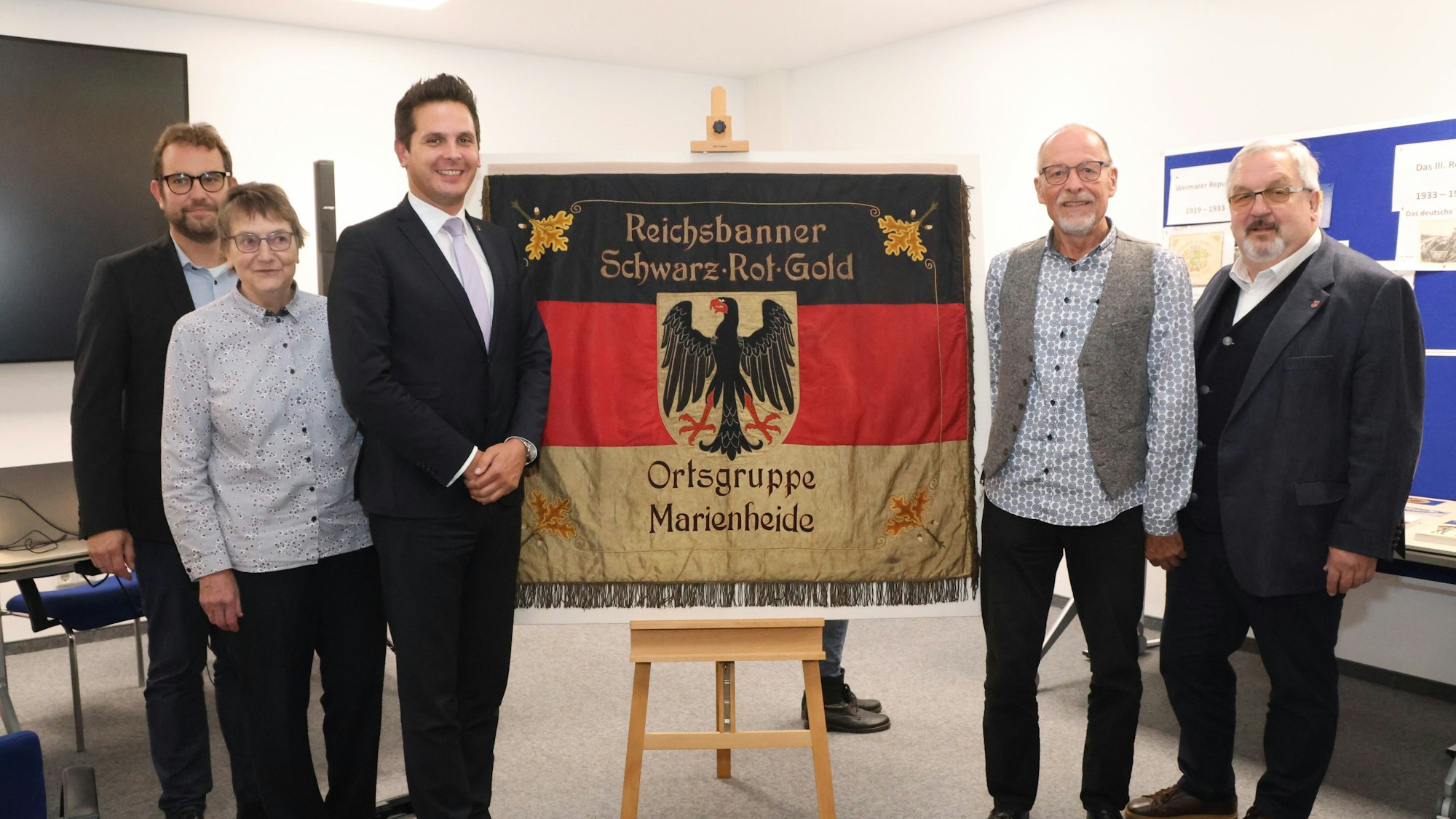 Vier Männer und eine Frau stehen um ein deutsches Reichsbanner herum.