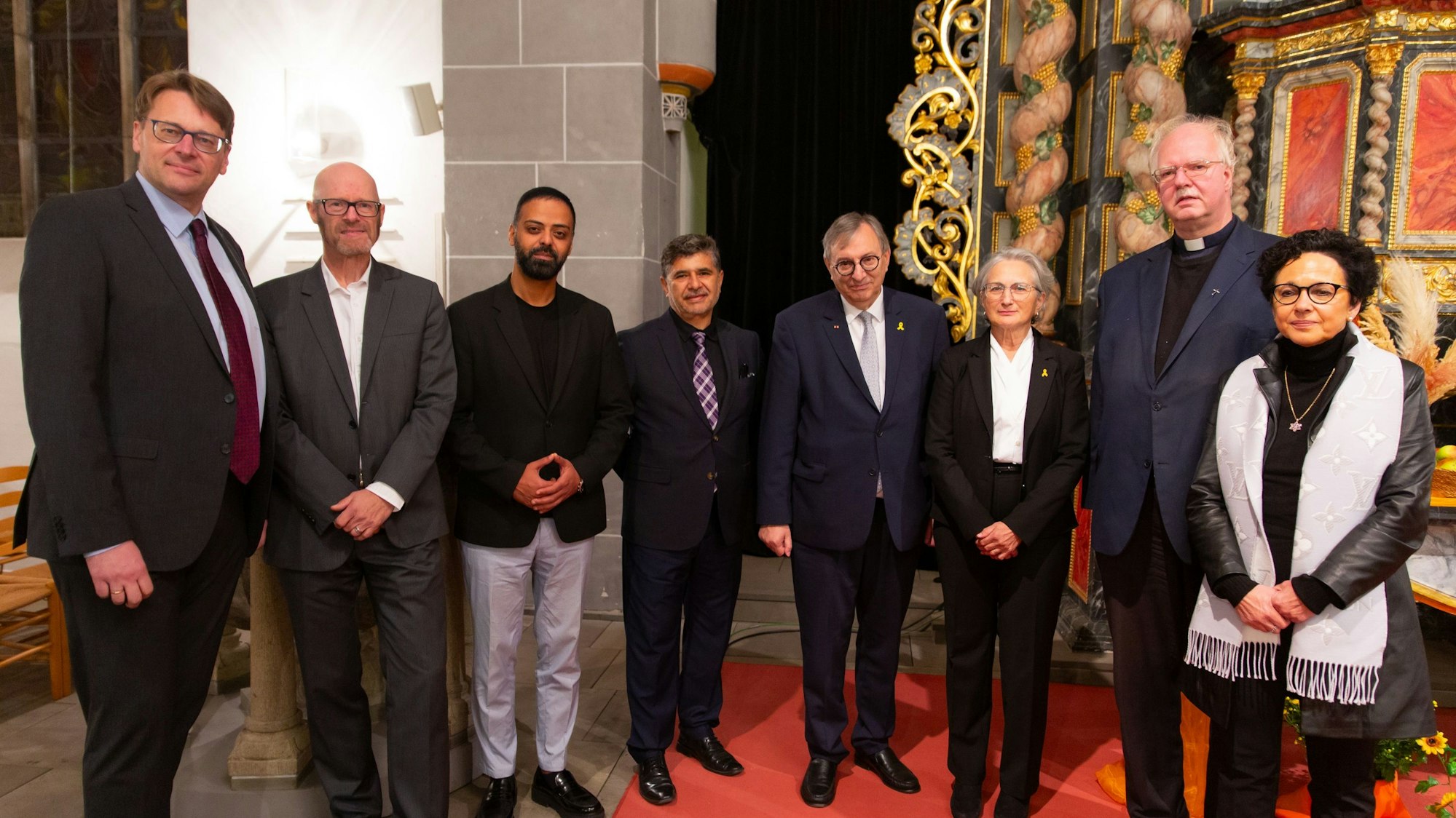 Zahlreiche Männer und einer Frau unterschiedlicher Religionen stehen bei einer Gedenkstunde in einer Kirche beisammen.