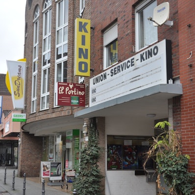 Zu sehen ist ein Gebäude aus Backstein, ein gelbes Schild weist auf ein Kino hin.