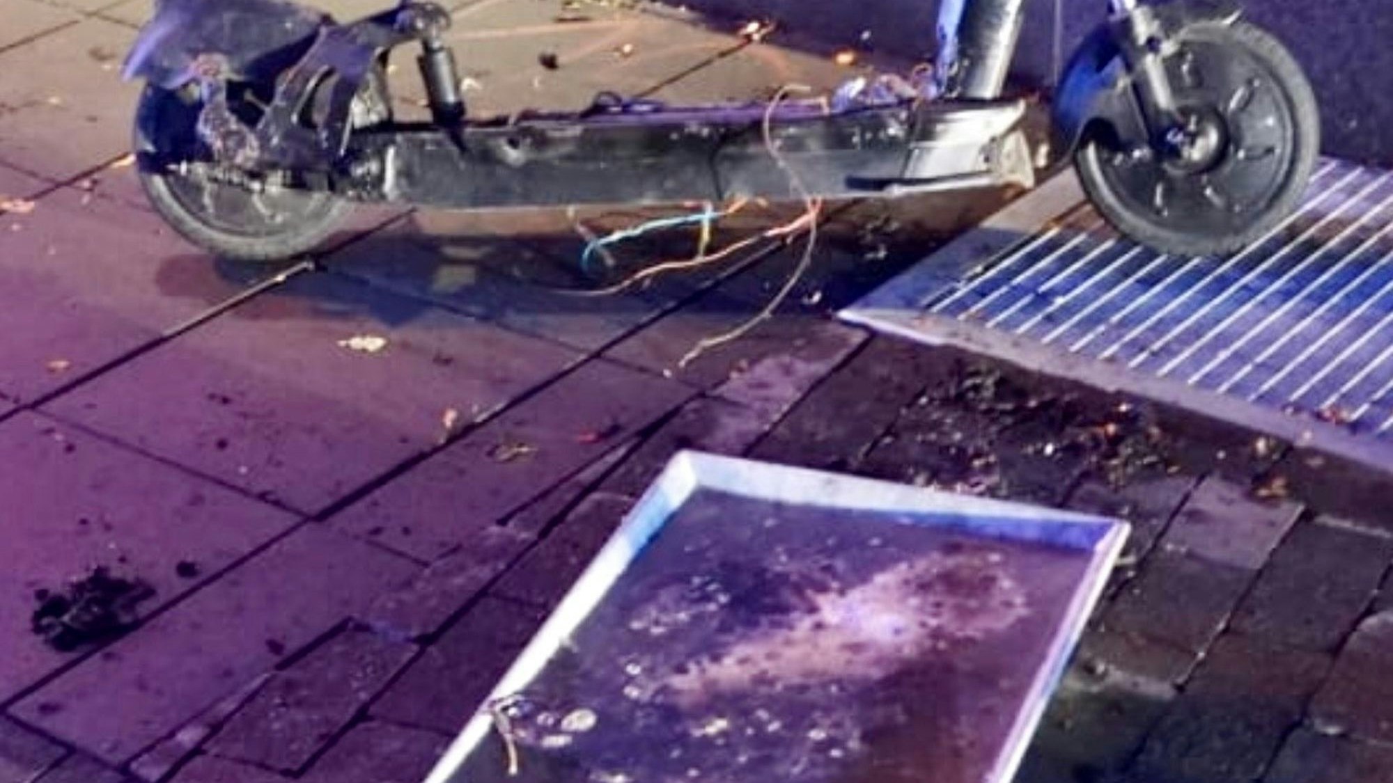 Das Bild zeigt die Wanne, in der der Akku gekühlt wird. Im Hintergrund ist der stark beschädigte E-Scooter zu sehen.