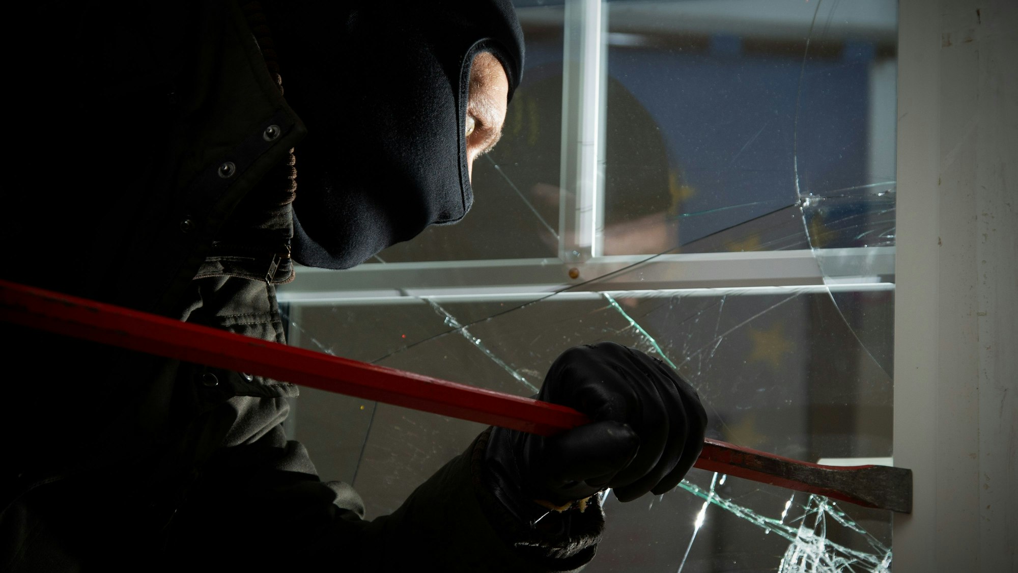 Ein maskierter Mann hebelt mit Einbruchswerkzeug eine Tür auf