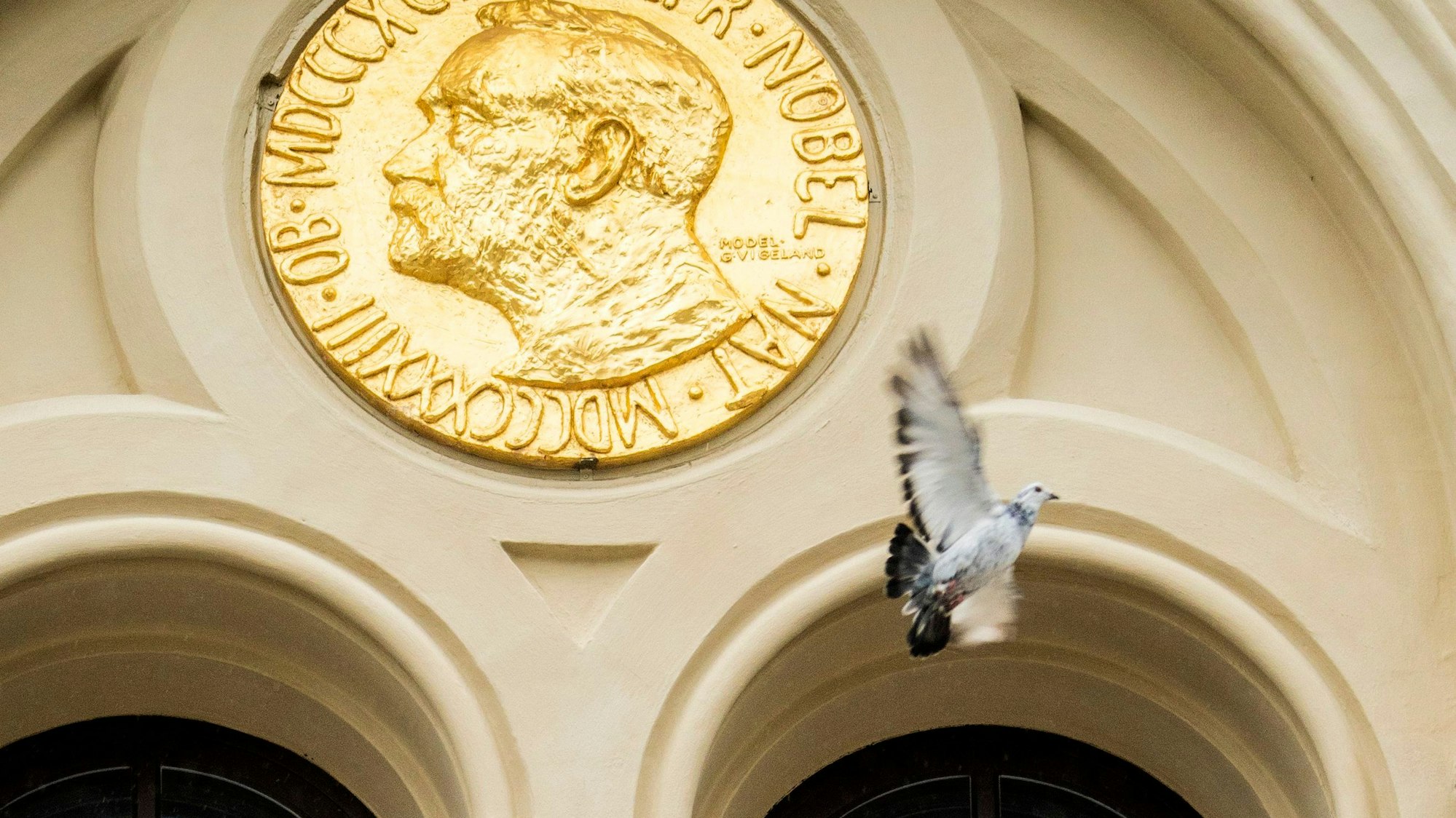 Eine Taube fliegt an einem Eingang vorbei, an dem eine große Münze mit dem Gesicht von Nobel angebracht ist, vorbei.