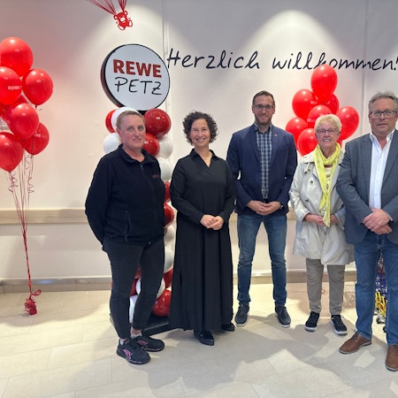 Fünf Menschen stehen zu einem Gruppenfoto aufgestellt vor weißen und roten Luftballons.