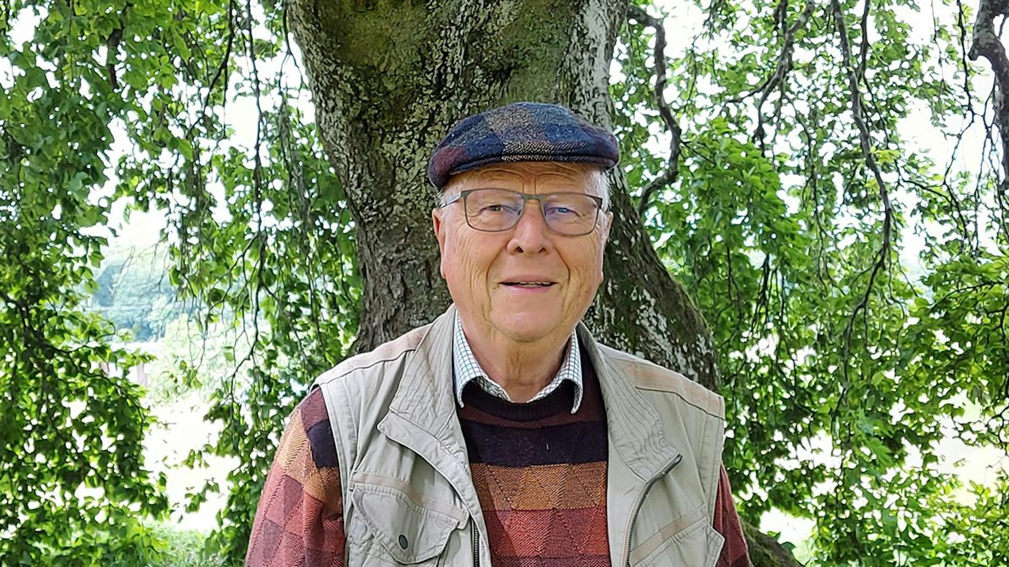 Das Bild zeigt Wolfgang Schumacher vor einem Baumstamm.