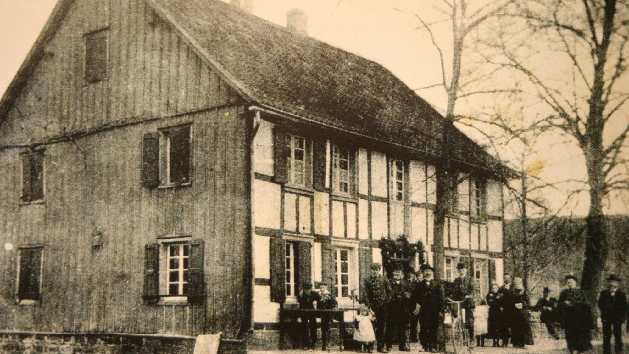 Ein schwarz-weiß-Foto eines Fachwerkhauses, Menschen stehen davor.