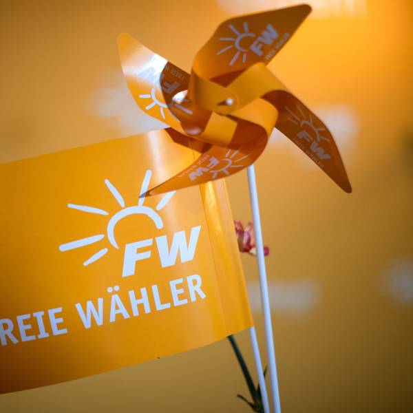 Ein orangefarbenes Fähnchen mit dem Aufdruck „Freie Wähler“ steht neben einem orangefarbenen Windrädchen.