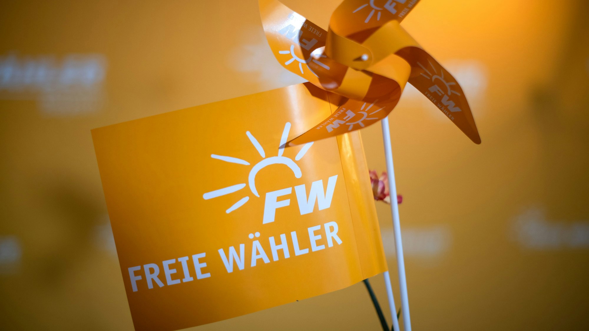 Ein orangefarbenes Fähnchen mit dem Aufdruck „Freie Wähler“ steht neben einem orangefarbenen Windrädchen.