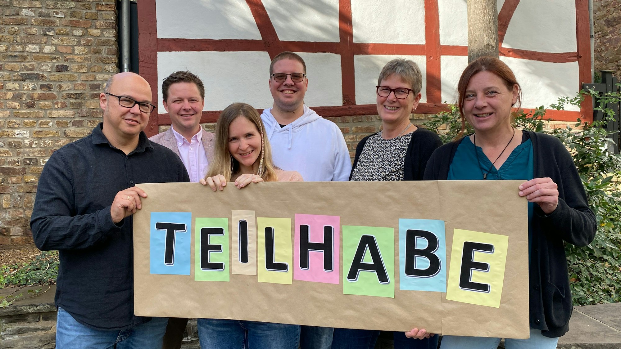 Eine Gruppe Menschen hält ein Plakat in die Kamera, auf der in Großbuchstaben Teilhabe steht.