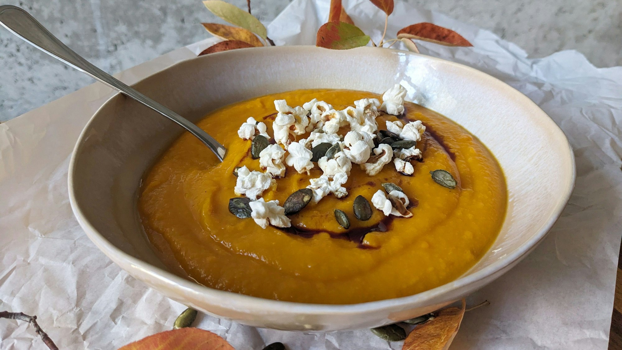 Eine Schüssel mit Kürbissuppe, die mit Popcorn, Kürbiskerne und Kürbiskernöl verziert ist.