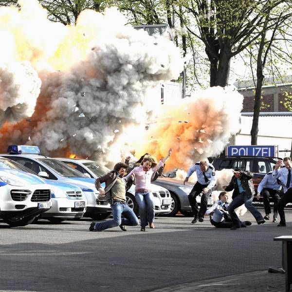 Das Foto zeigt eine Filmexplosion in der Kulisse der Autobahnpolizeiwache. Davor mehrere Polizeiautos und flüchtende Menschen.