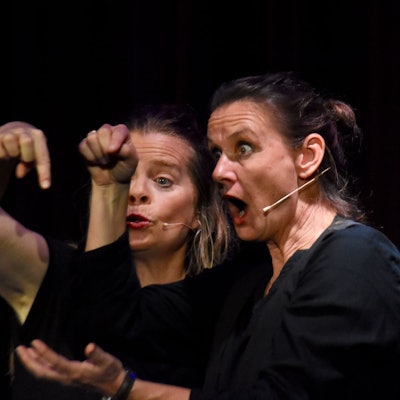 Zwei Frauen gestikulieren vor einem schwarzem Hintergund.