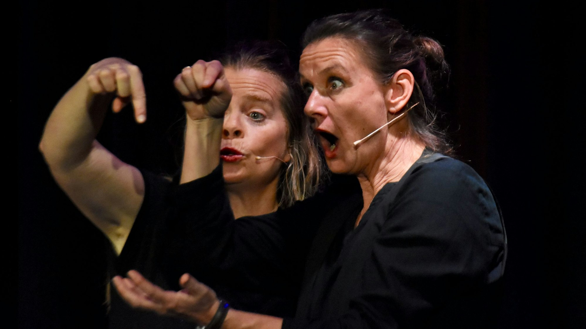 Zwei Frauen gestikulieren vor einem schwarzem Hintergund.