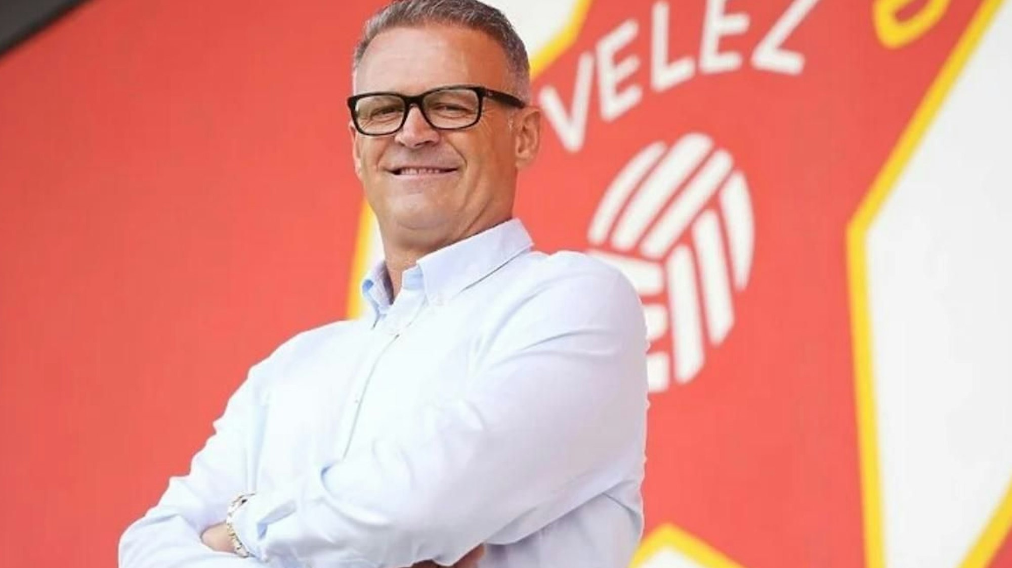 Foto eines Fußballtrainers vor einem Vereinslogo