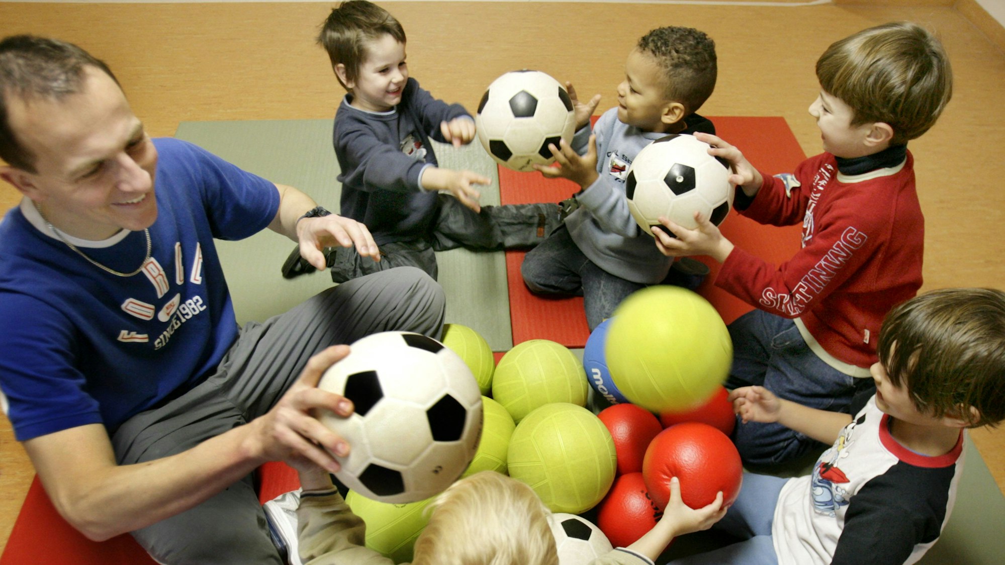Kindergartenkinder und ein Erzieher spielen in einer Kita mit Fußbällen (Symbolbild).