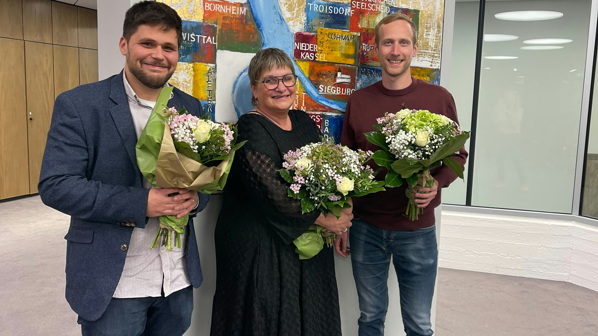 Zwei Männer und eine Frau mit Blumensträußen.