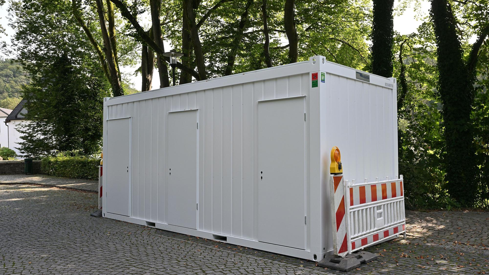 Ein weißer Toilettencontainer steht auf dem Parkplatz nahe dem Altenberger Dom.