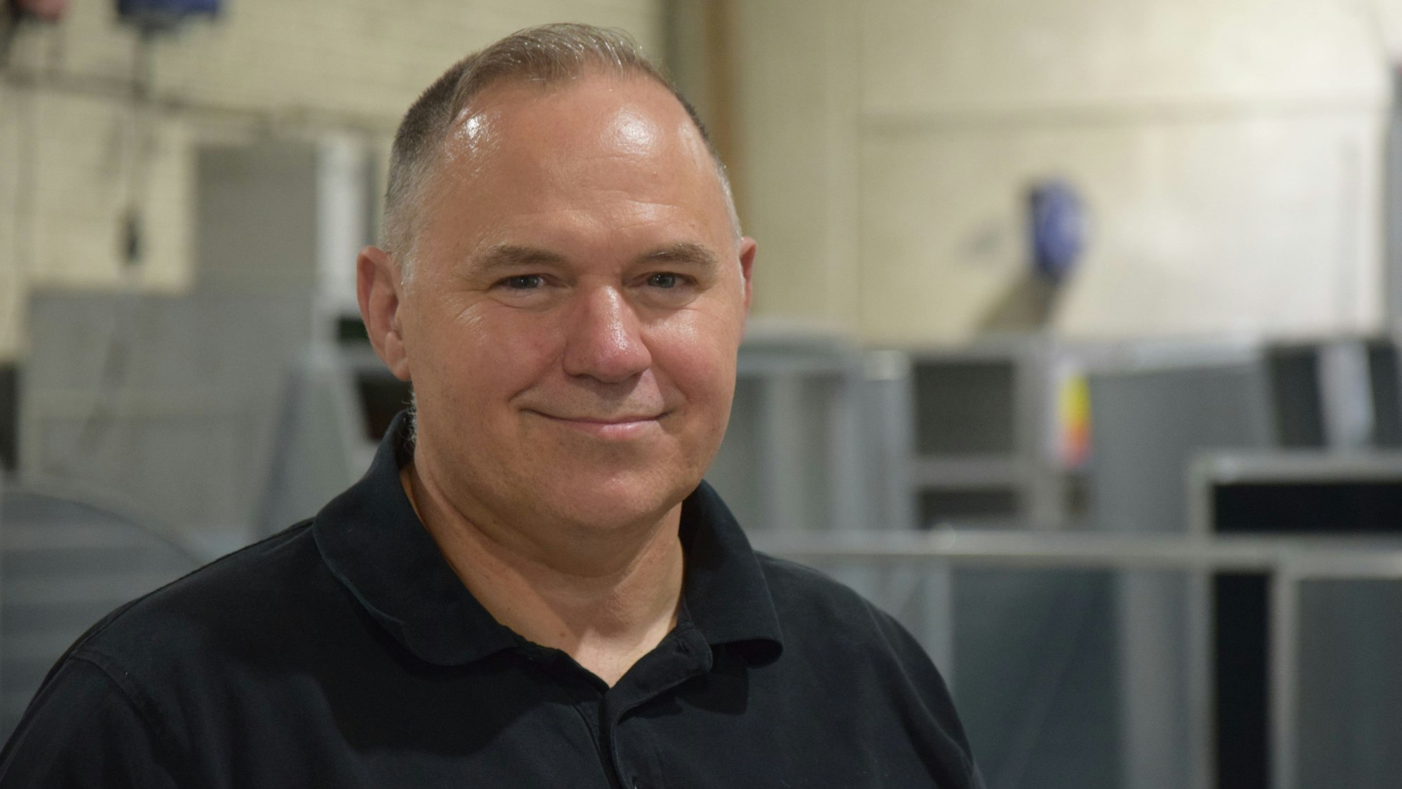 Mann mit dunklem Polo-Shirt lächelt in die Kamera.