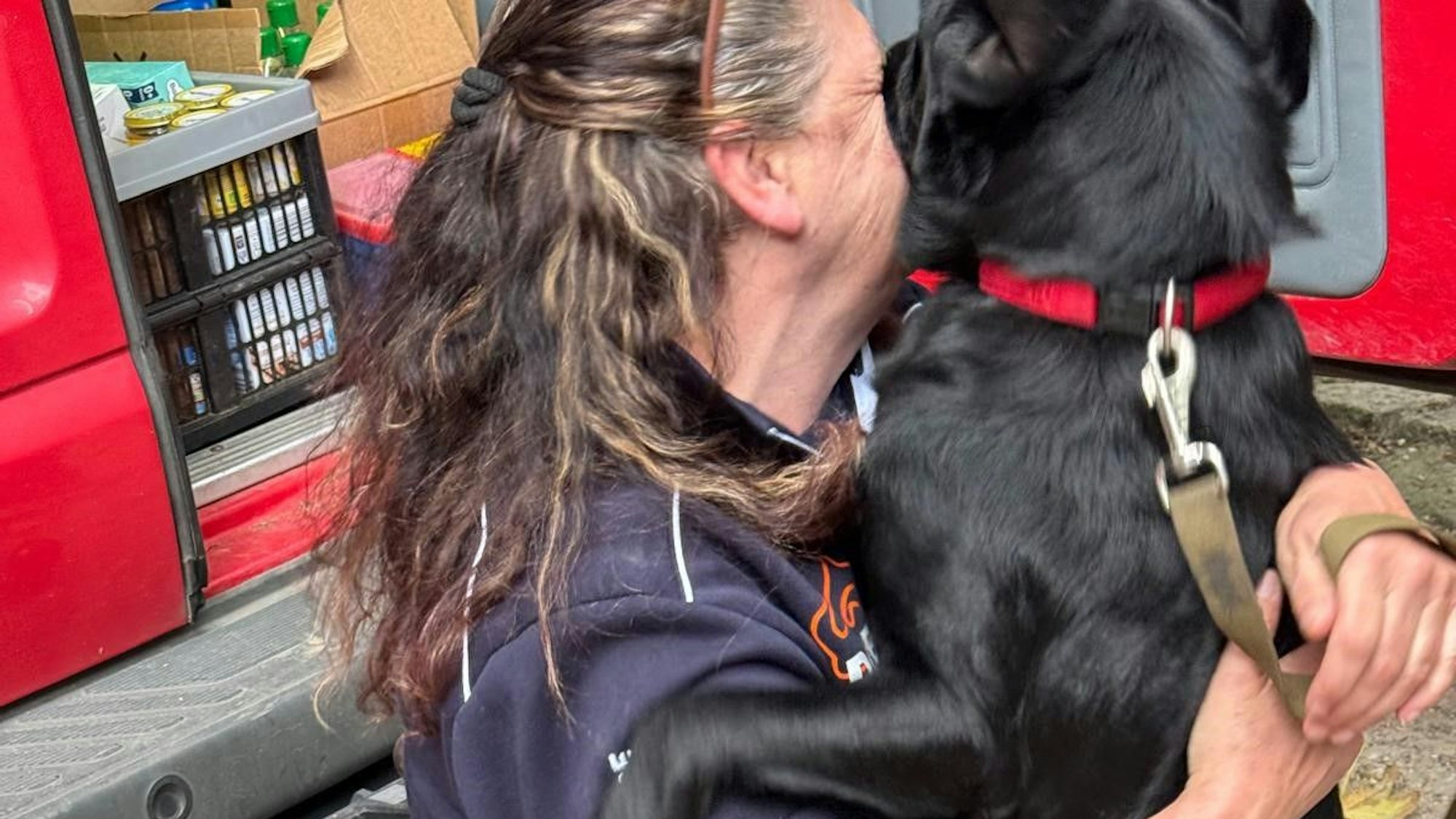 Das Bild zeigt einen schwarzen Hund, der eine Fluthelferin freudig begrüßt.