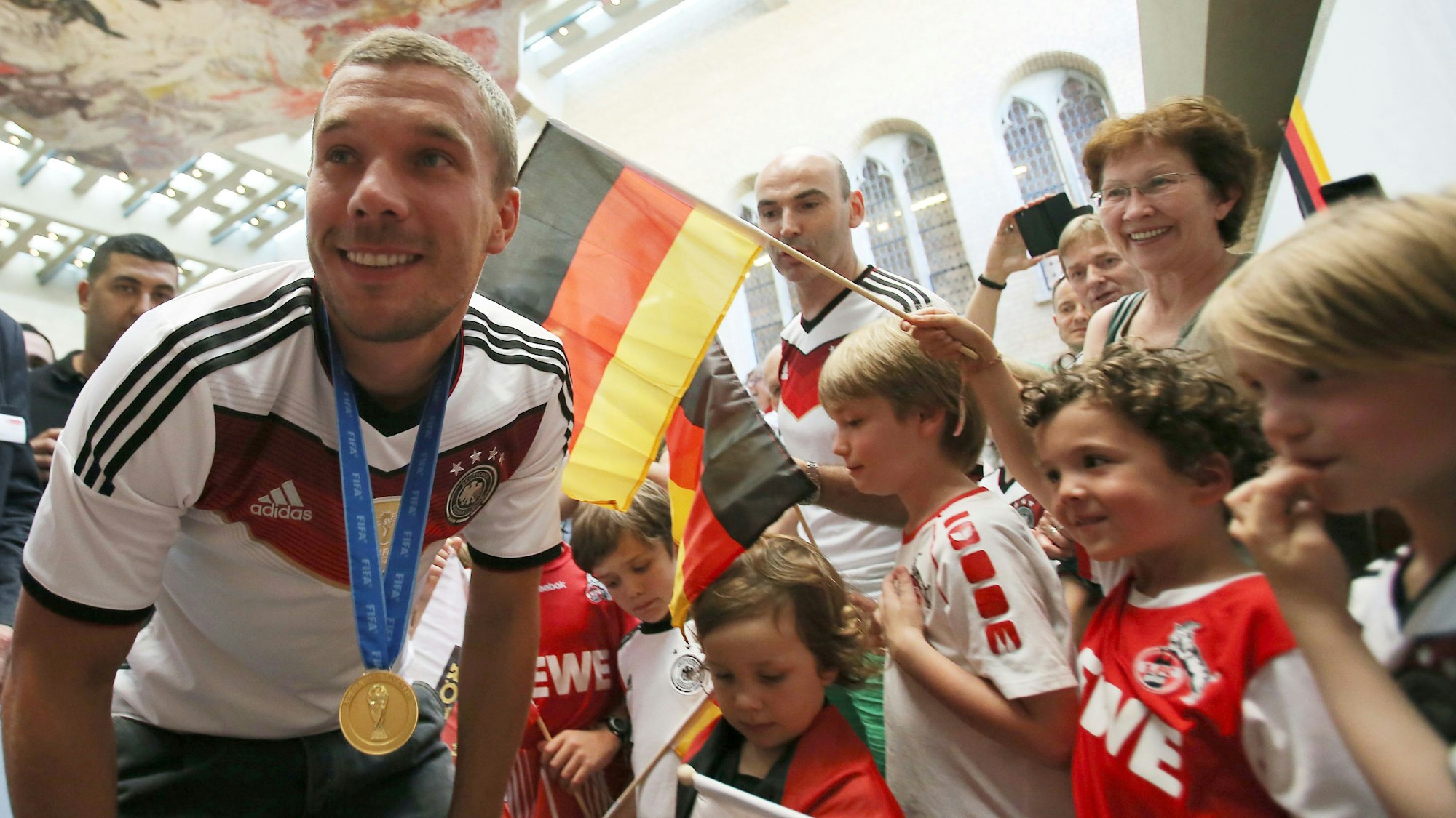 Fußball-Weltmeister Lukas Podolski spricht am16.07.2014 in Köln vor dem Rathaus mit Kindern. Um seinen Hals hängt die Goldmedaille der WM in Brasilien.